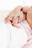Hands holding a newborn baby in bed
