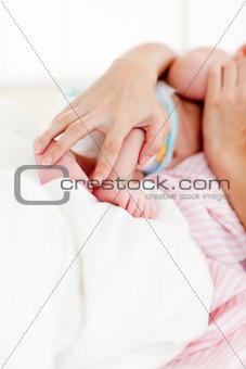 Hands holding a newborn baby in bed
