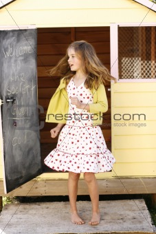 Pretty young girl spinning around outside her playhouse.