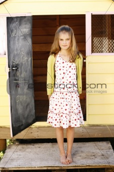 Portrait of a pretty young girl standing outside her playhouse.