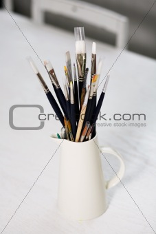 Set of paintbrushes in a jug on a table.