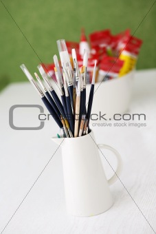 Set of paintbrushes and tubes of paint on a table outdoors.