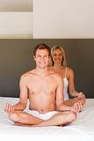 Smiling young couple doing yoga on bed