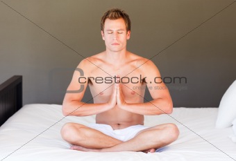Young boy doing yoga on bed with clossed eyes