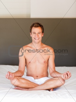 Smiling handsome man meditating on bed 