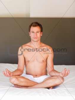 Young man doing yoga on bed