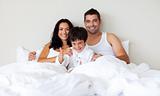 Kid with thumbs up and his parents in bed