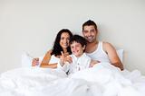 Child with thumbs up and his parents in bed