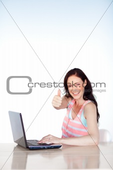 Smiling woman using a laptop with thumb up and copy-space