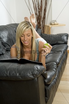 Female model relaxing on sofa reading magazine