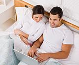 Couple Relaxing in Bed and Looking at a Laptop