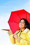 Beautiful young woman in raincoat with umbrella checking for rain