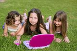 Three little girl playing with toy computer in grass