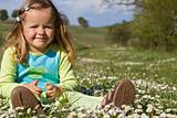 Little girl sitting among wildflowers on the field