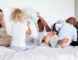 Parents and children playing with pillows on bed