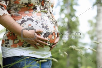 Woman holding her pregnant belly outdoors.