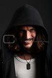 Young man in black hood with cheeky grin on black background