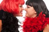 Red and Black Haired Women with Feather Boas Touching Noses and Smiling at Each Other.