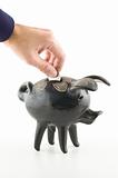 Hand dropping a coin into a black piggy bank