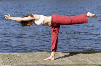 Lady performing the 'one foot' yoga pose by the water