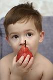 The boy eats a red pear