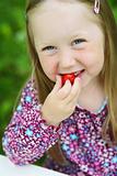 Smiling little girl eating a strawberry. 