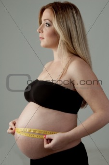 side pose of pregnant female measuring her belly