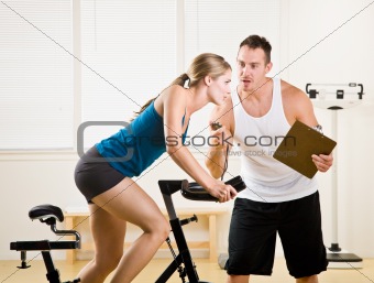 Trainer timing woman on stationary bicycle