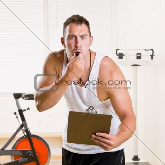 Personal trainer blowing whistle in health club