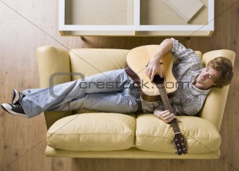 Man laying on sofa playing guitar