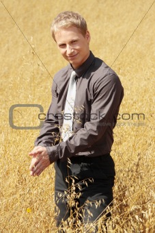 Farmer in suit standing in field of oats