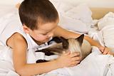 Little boy caressing his kitten in bed