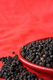pile of black pepper on red background