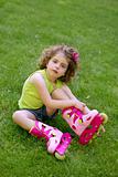 Little girl sit on the grass with roller skates