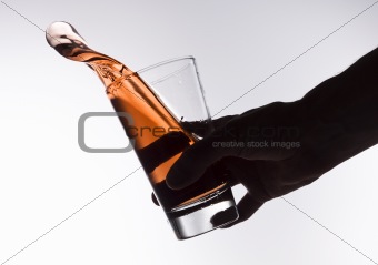 Silhouette of an hand holding a red glass with splashing lemonade