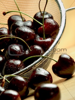 Dark cherries in steel mesh sieve on wooden table under warm lighting
