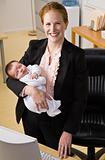 Businesswoman holding baby at desk