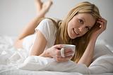 Woman Reclining in Bed With a Coffee Cup In Her Hand