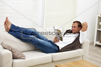 smiling young man on a couch reading a book