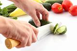 Someone cutting a cucumber, and slice flying isolated on white