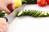   Someone cutting a cucumber, and slice flying isolated on white