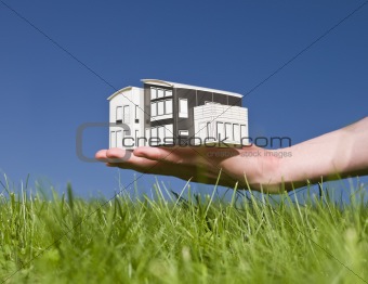 Man holding a miniature house outside in the sun.