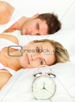 Woman lying with her boyfriend looking at the alarm clock 