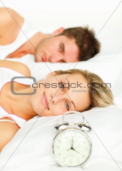 Couple in bed with alarm clock and woman smiling at the camera