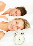 Couple in bed with alarm clock and woman smiling at the camera