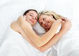 Couple lying in bed and smiling at the camera