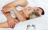 Couple in bed with alarm clock going off