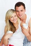 Couple in bed drinking coffee and smiling at the camera