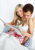 Happy couple reading a newspaper in bed