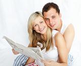 Couple reading a newspaper in bed and smiling at the camera